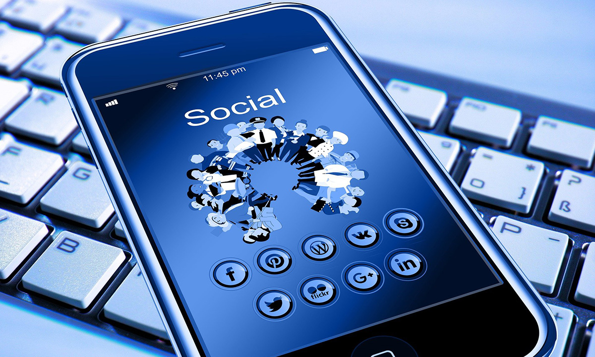Das Bild trägt den Titel "network". Es zeigt ein eingeschaltetes Smartphone, welches auf einer Computertastatur liegt. Auf dem Display des Smartphones steht der Text "Social" und die Schaltflächen von verschiedenen SocialMedia-Diensten sind zusätzlich abgebildet.